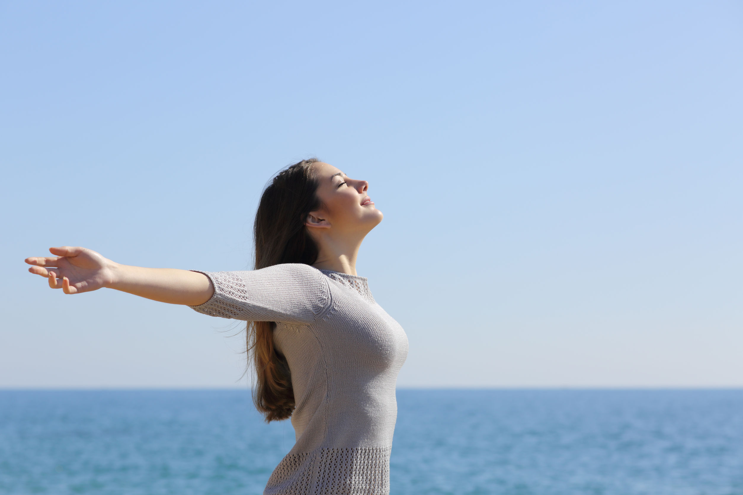 Happy woman breathing deep fresh air and raising arms on the beach